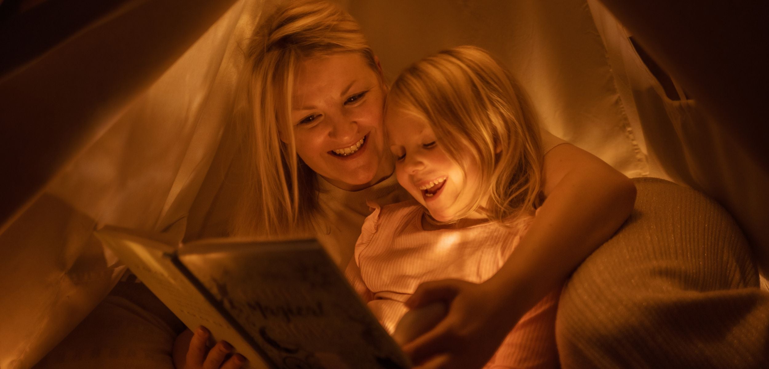 Eine Mutter liest ihrer kleinen Tochter aus einem Buch vor. Das HerzLicht dient als charmantes Leselicht.