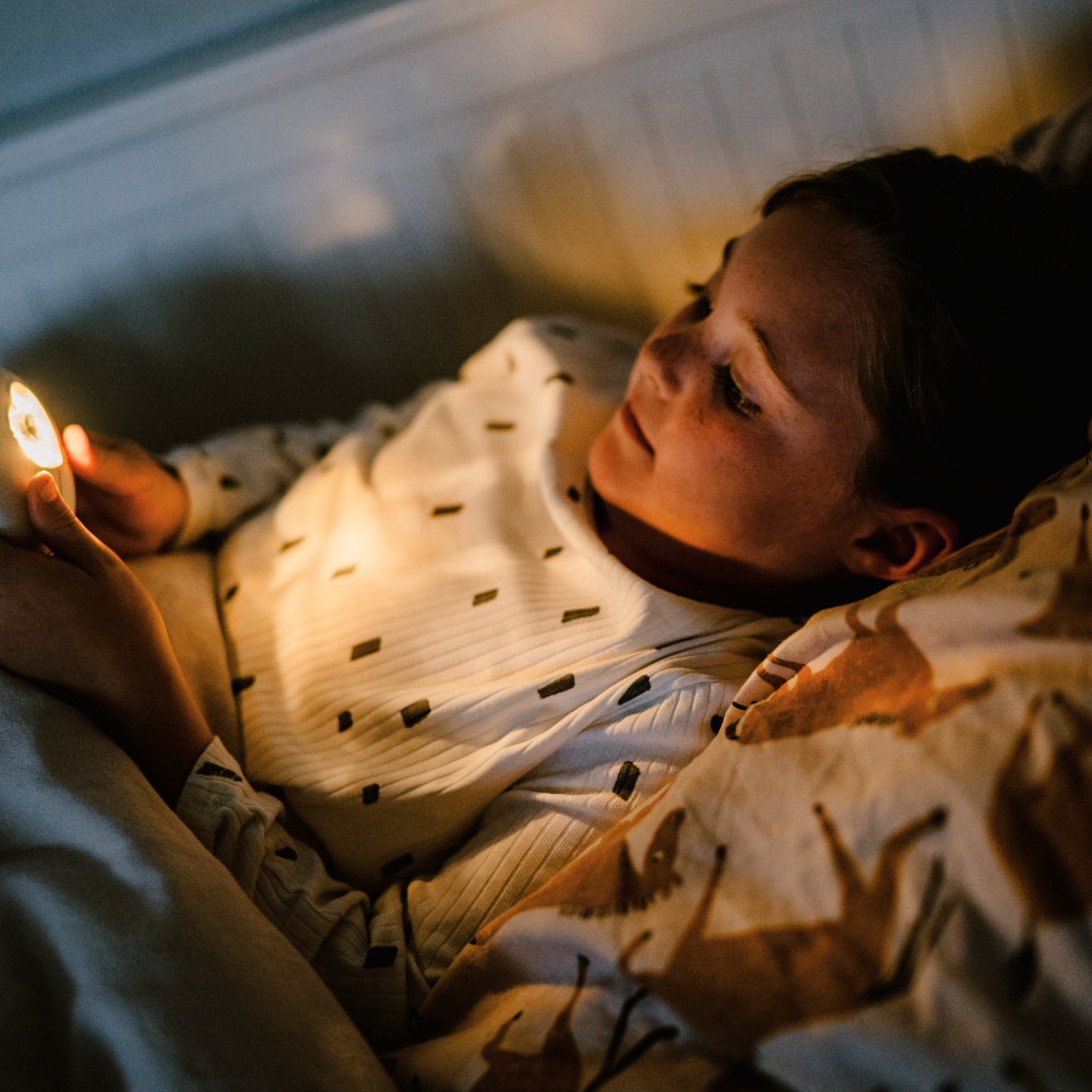 Ein Mädchen liegt im Bett und betrachtet fasziniert das leuchtende HerzLicht.