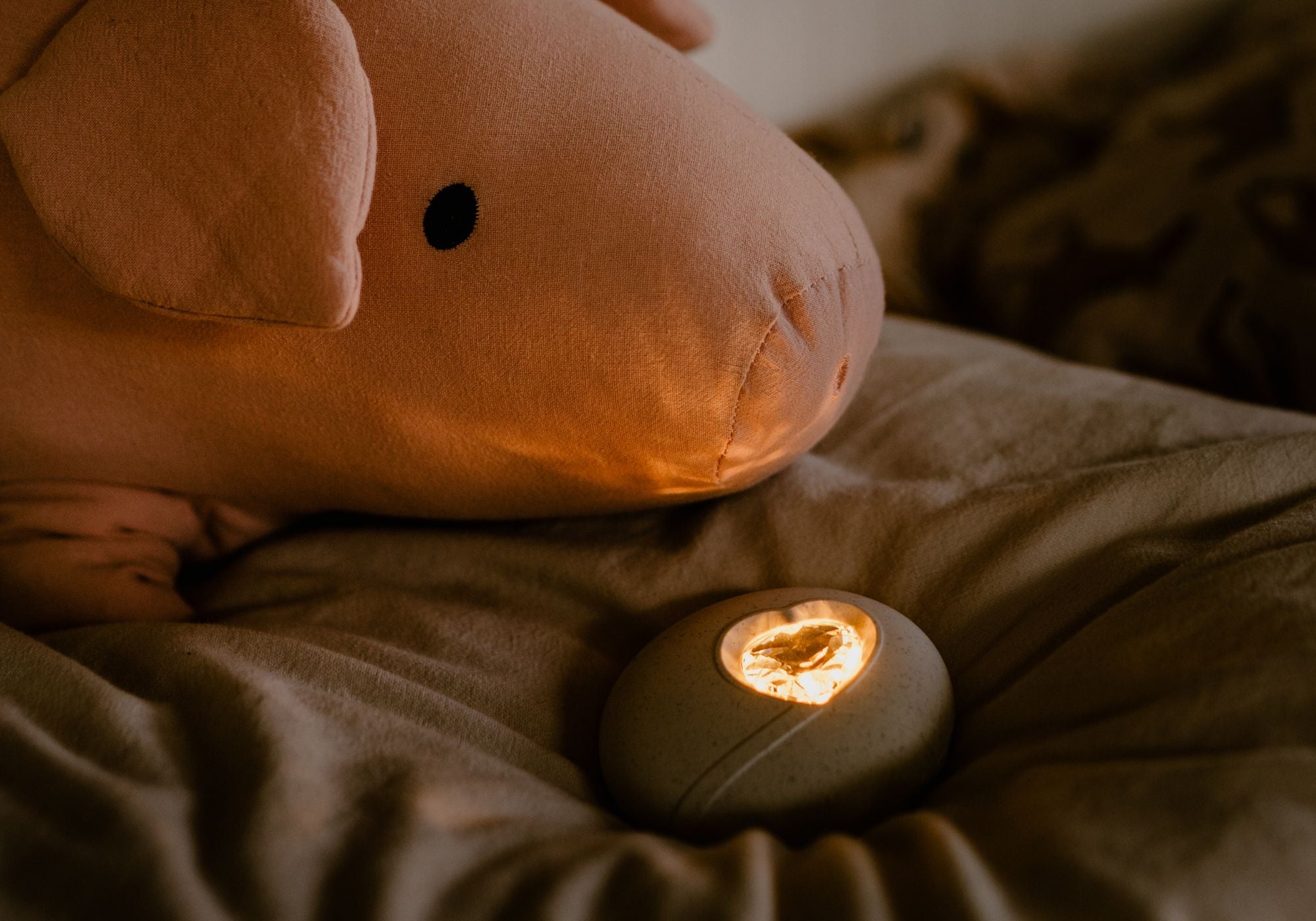 Das HerzLicht funkelt und liegt auf der Couch neben einem Kuscheltier.